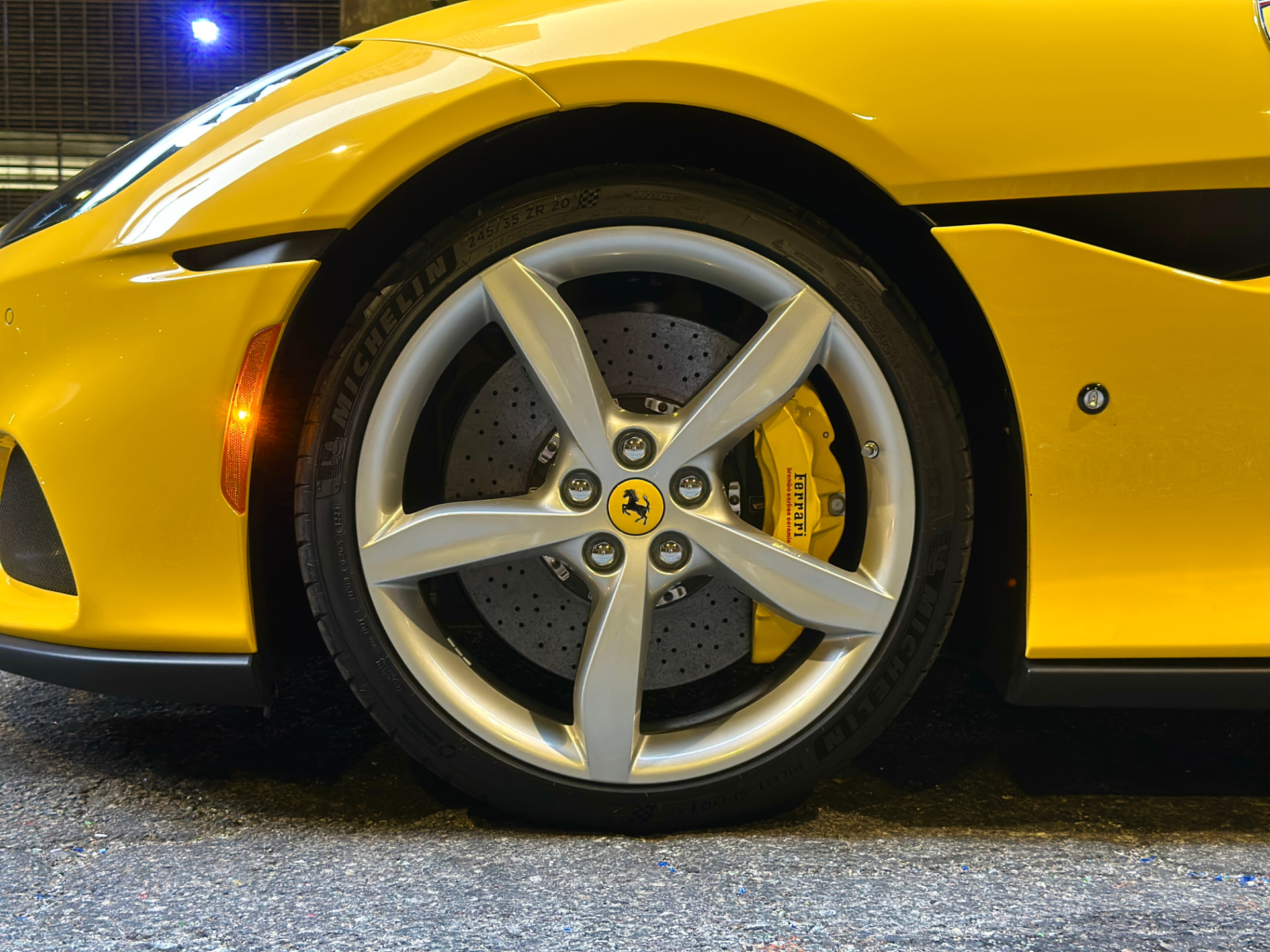 Close-up of the front wheel on a yellow Ferrari: silver five-spoke alloy, Michelin tyre, drilled brake rotor and a yellow Ferrari-branded brake caliper